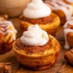Pumpkin Pie Cinnamon Roll Cups on table with whipped cream on top of some and a icing glaze on others
