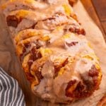 Pumpkin Pie Pull Apart Bread on a cutting board sitting on table with glaze drizzled on top