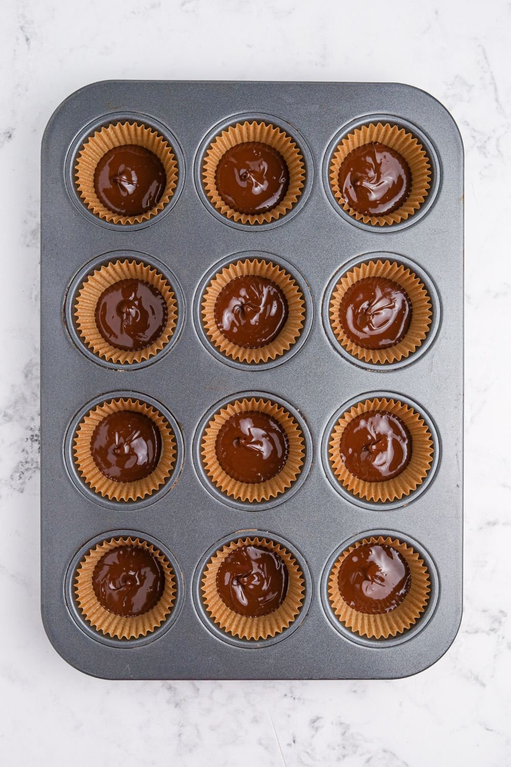 chocolate poured into muffin cup with a liner to make Peanut Butter Marshmallow Cups