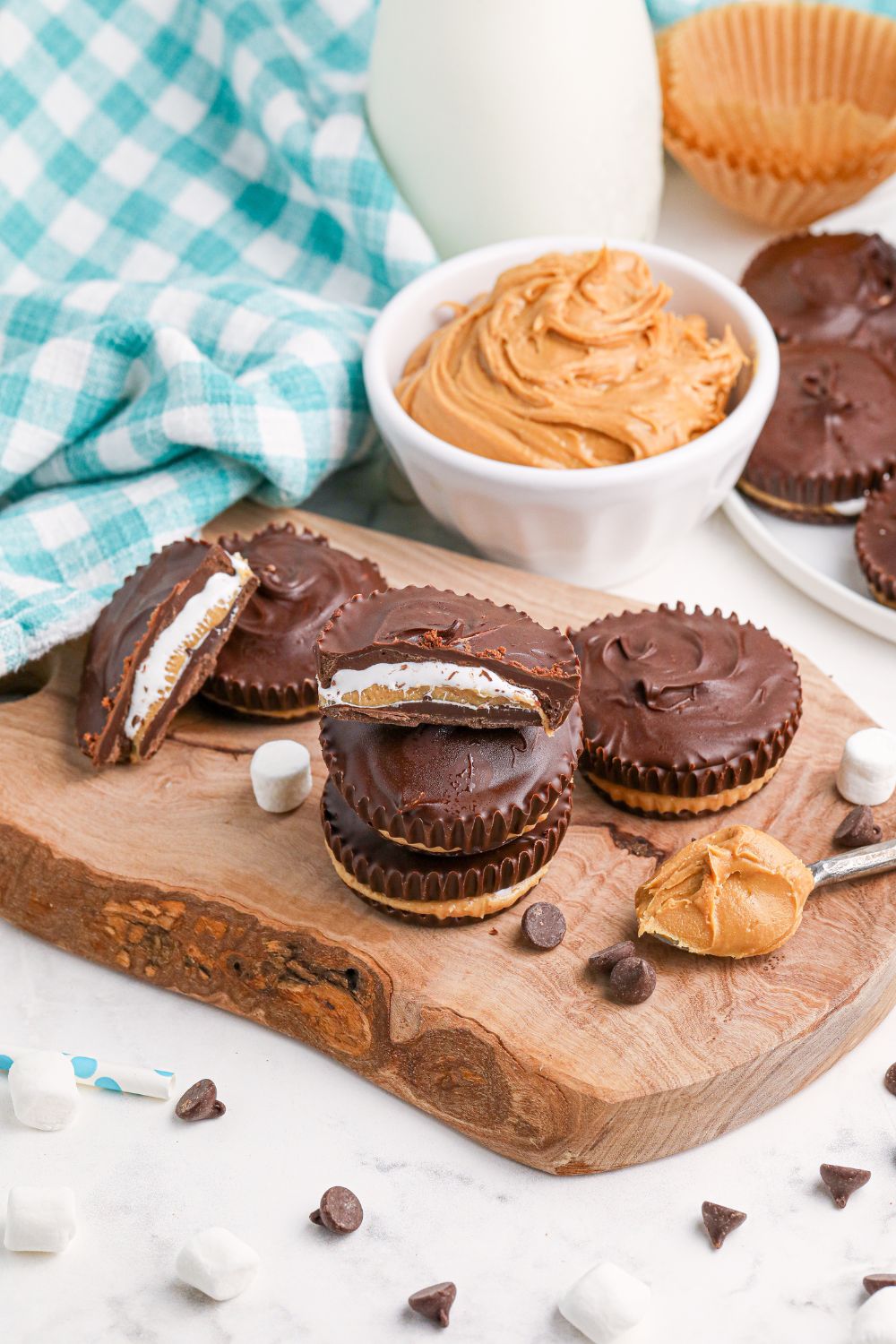 Peanut Butter Marshmallow Cups on table with a bowl of peanut butter behind it and on a spoon next to the cups 