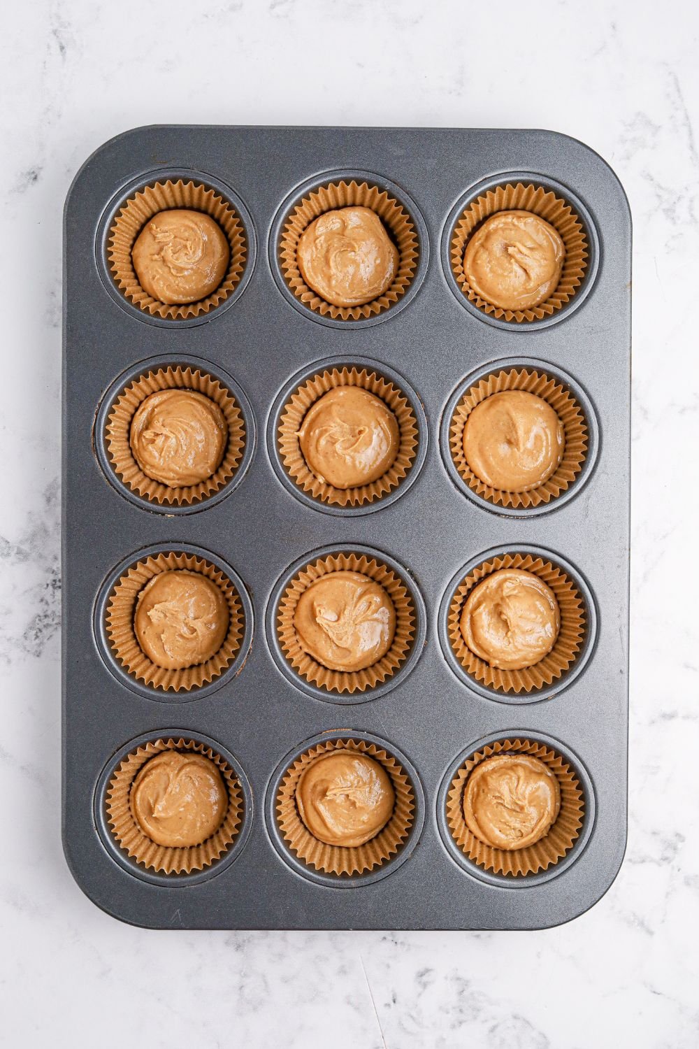 peanut butter poured over chocolate in muffin tin for making Peanut Butter Marshmallow Cups