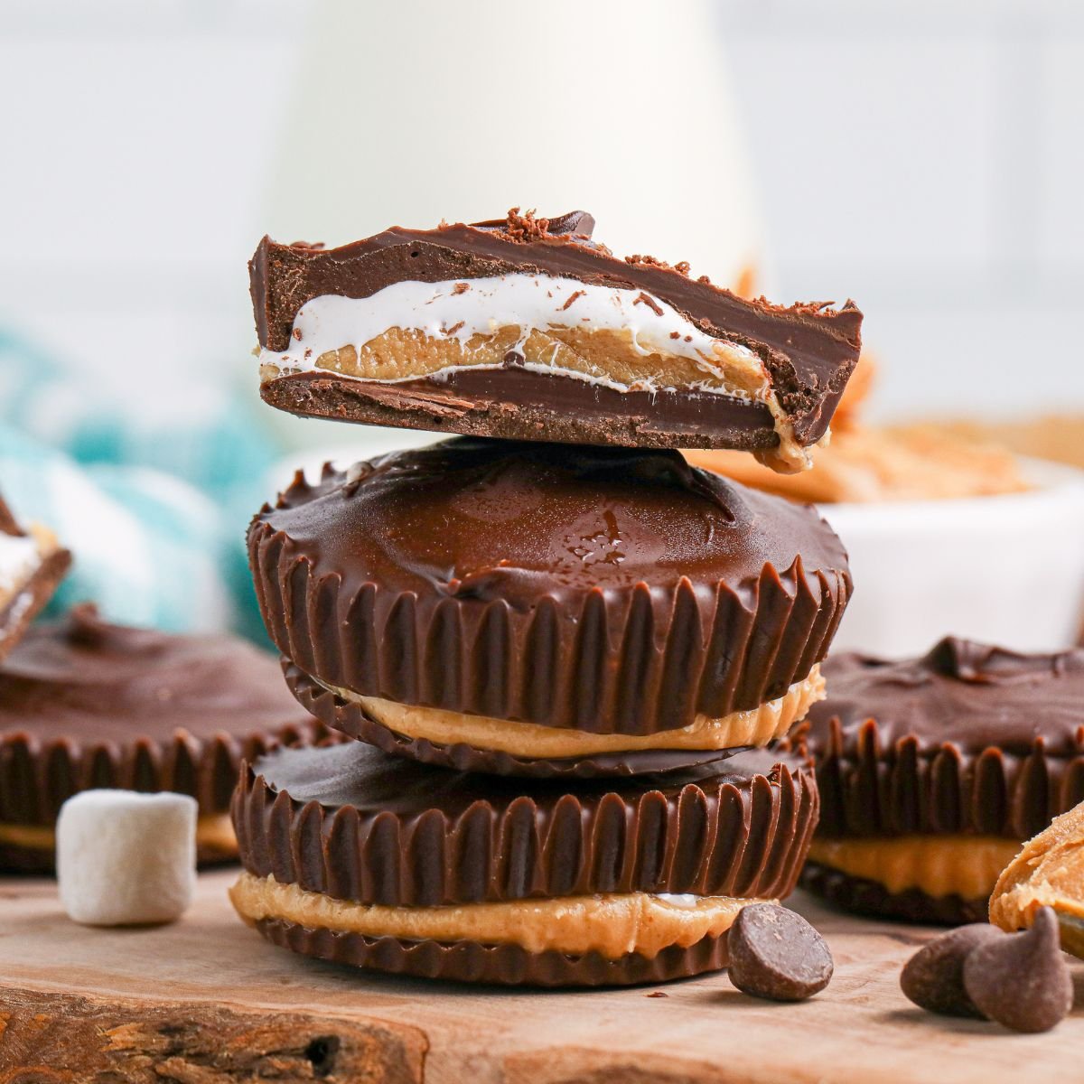 Peanut Butter Marshmallow Cups stacked on wooden cutting board with top one cut in half so you can see the layers