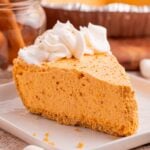 Slice of Marshmallow Pumpkin Pie on plate with a few crumbs from crust sprinkled on around the table