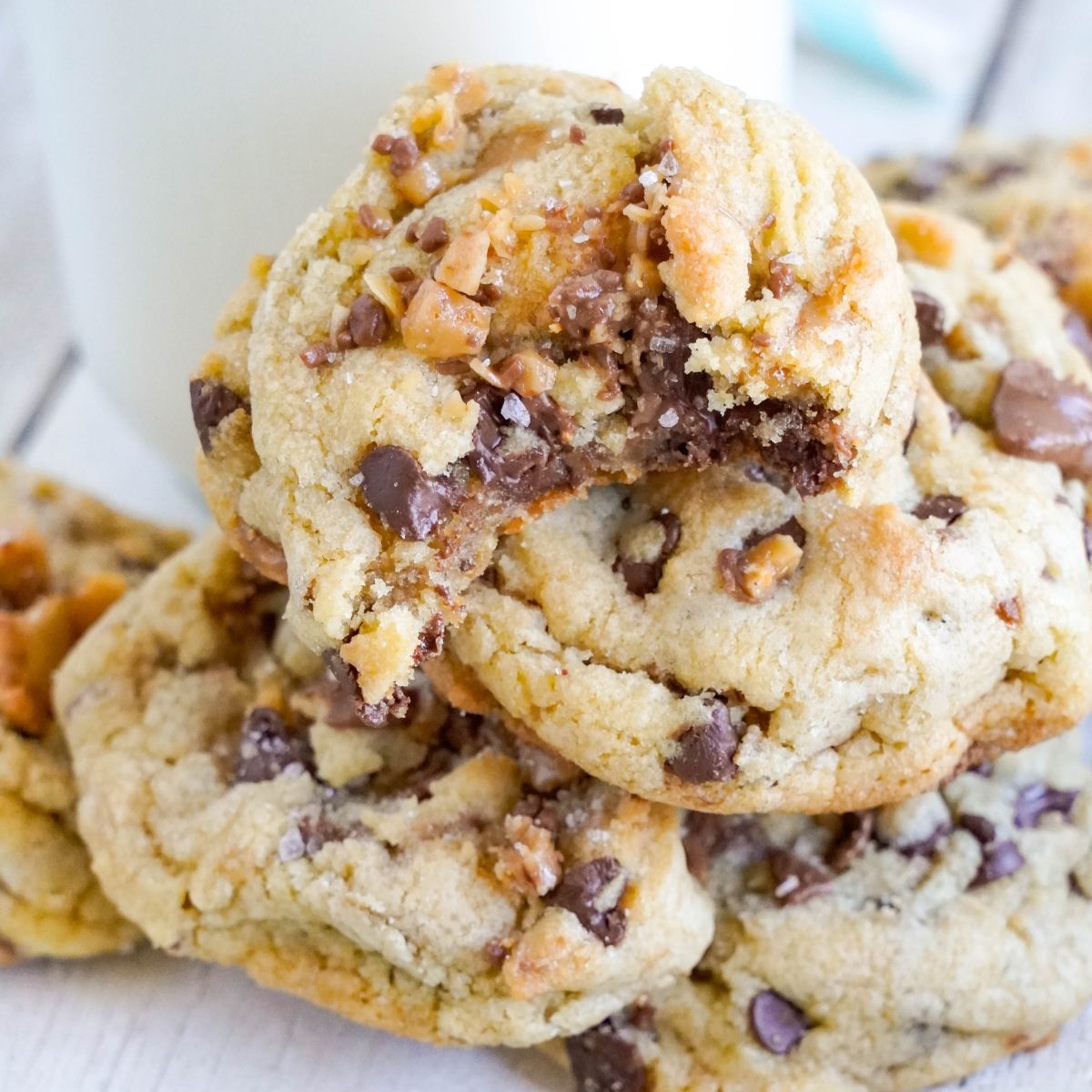 Chocolate Chip Toffee Cookies stacked on top of each other on table with a glass of milk on table 