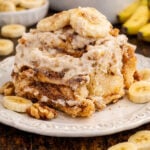 Banana nut cinnamon roll on a white plate with sliced bananas