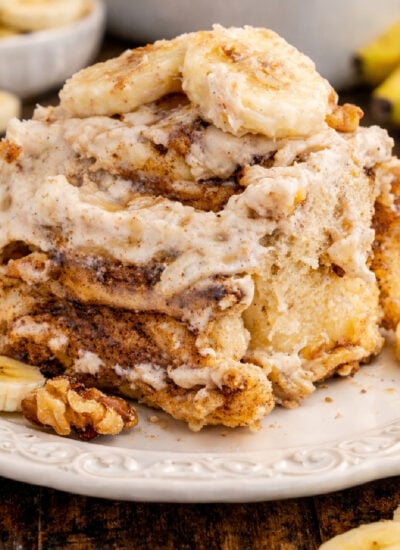 Banana nut cinnamon roll on a white plate with sliced bananas