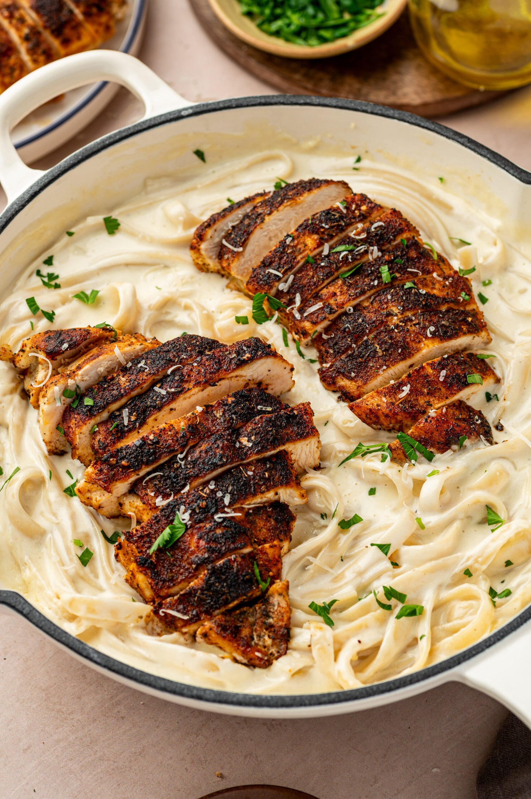 blackened chicken alfredo in a baking dish with parsley and grated parmesan cheese on top