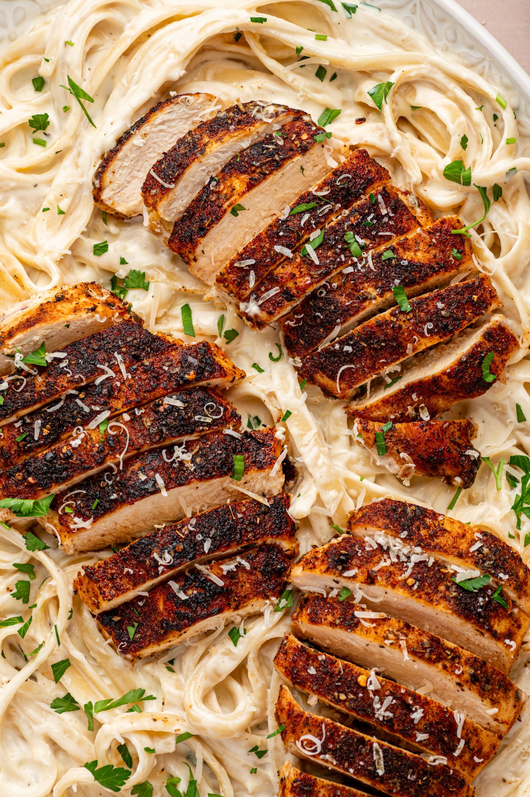blackened chicken alfredo on a plate with parsley and grated parmesan cheese on top