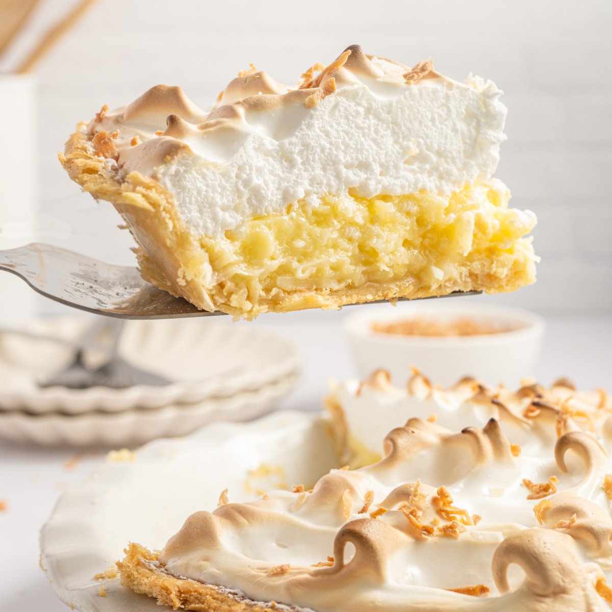 Coconut Meringue Pie in pie plate with a pie spatula lifting out a slice