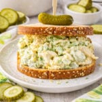 Pickle Chicken Salad on bread sitting on a plate with a pickle sitting on the top of the bread