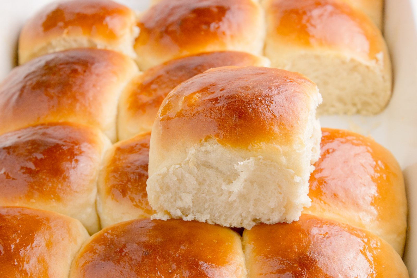 Hawaiian dinner rolls in a baking dish with one removed sitting on top