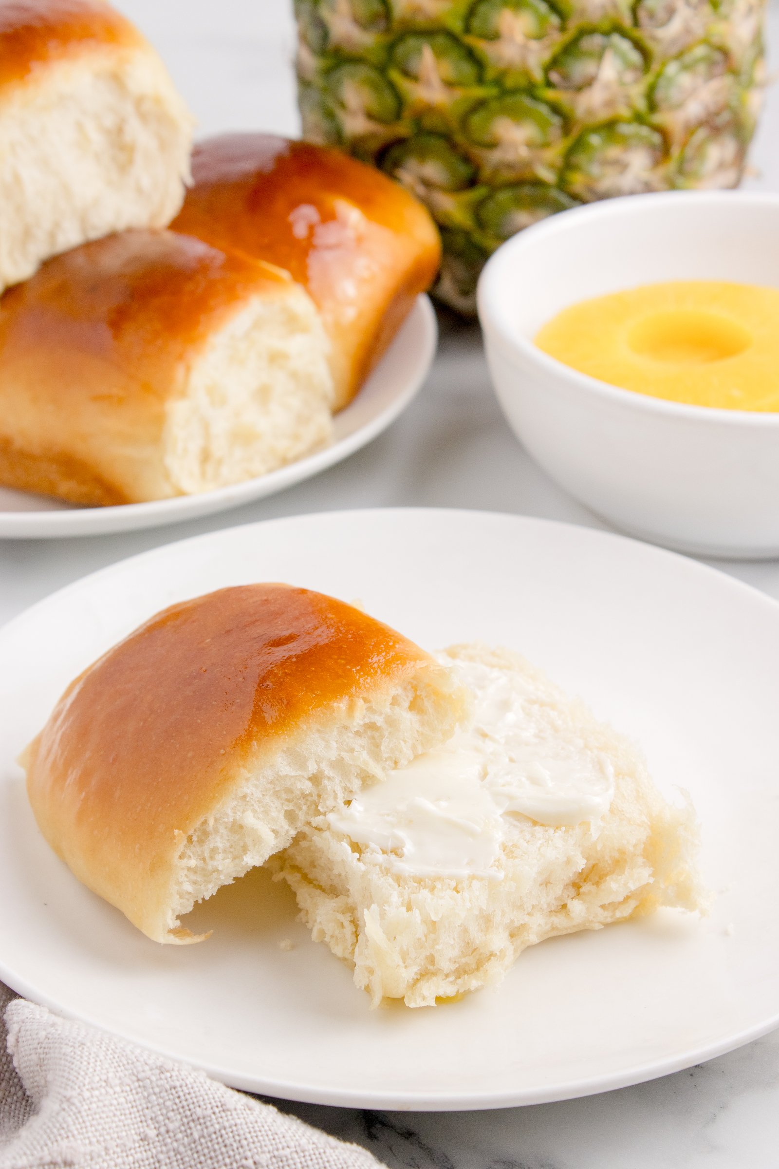 Hawaiian Dinner Roll on plate with it sliced in half and butter spread on it 