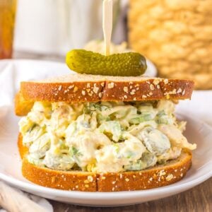 Pickle Chicken Salad on bread sitting on a plate with a pickle sitting on the top of the bread