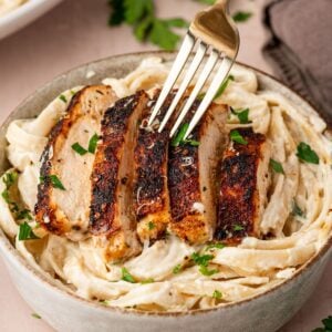 Blackened Chicken Alfredo in a bowl with a fork poking into the chicken