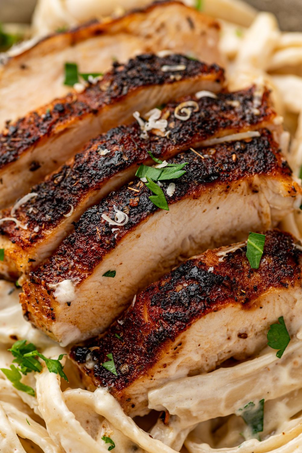 blackened chicken alfredo on a plate with parsley and grated parmesan cheese on top