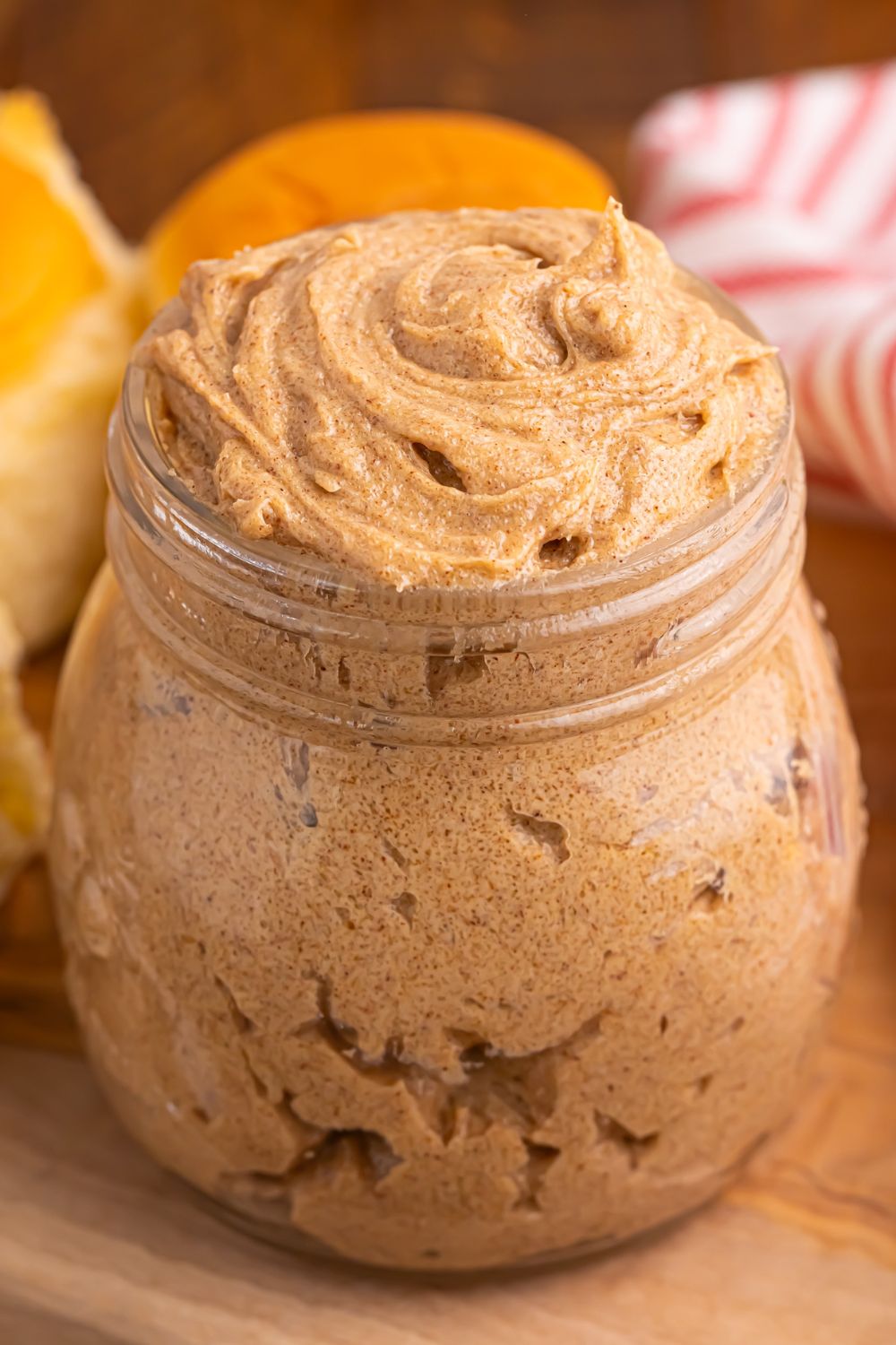 Brown Sugar Cinnamon Butter in a jar on a wooden cutting board on table with dinner rolls behind the jar 