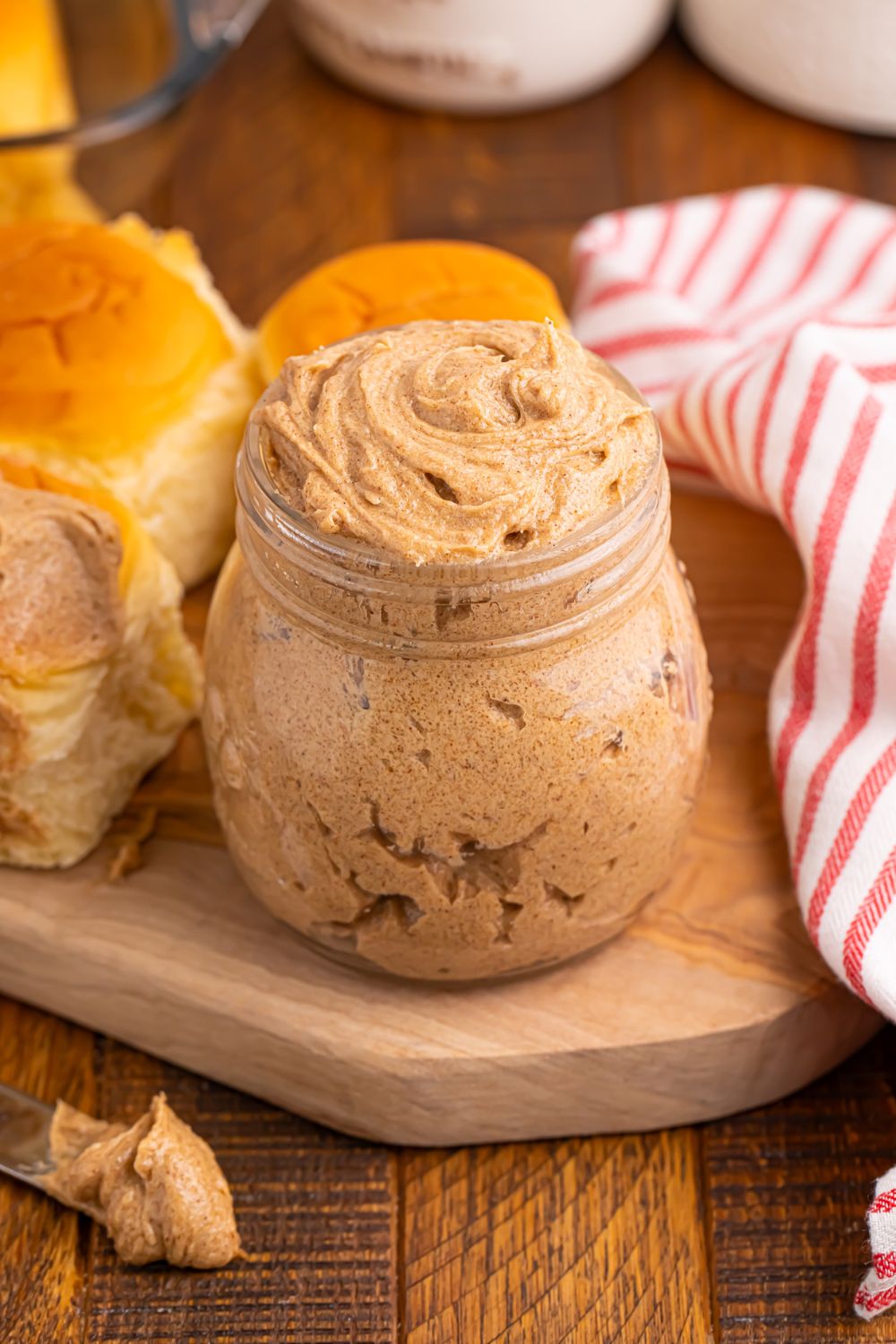 cinnamon spread in a jar with rolls and a towel around it on table