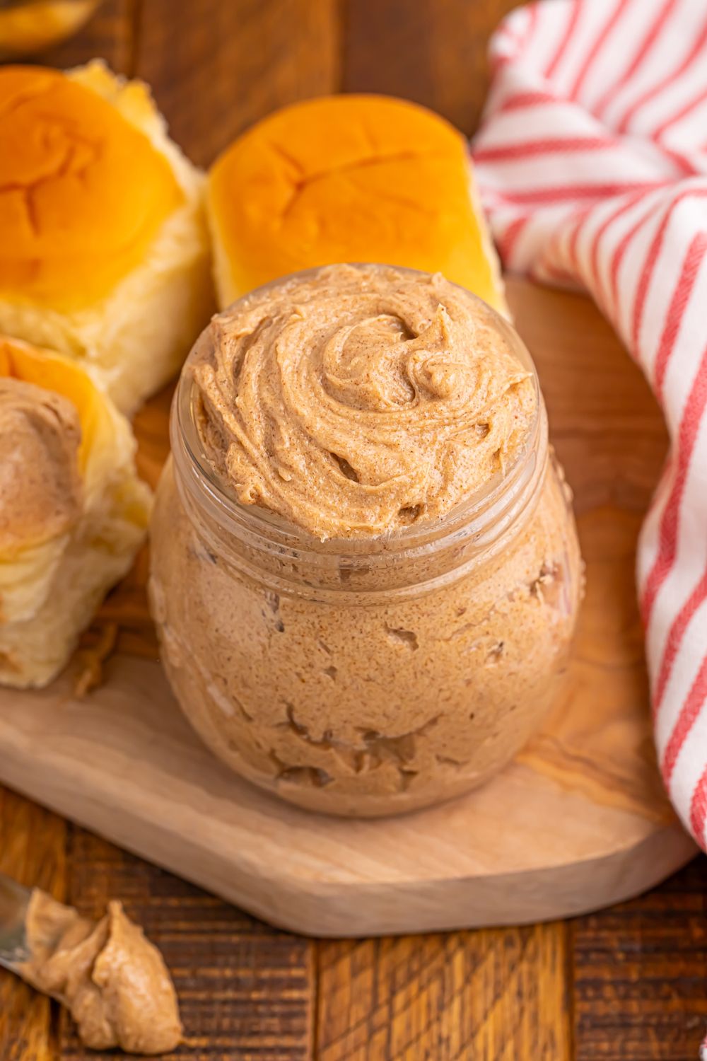 homemade cinnamon butter in a glass jar with rolls around it on table