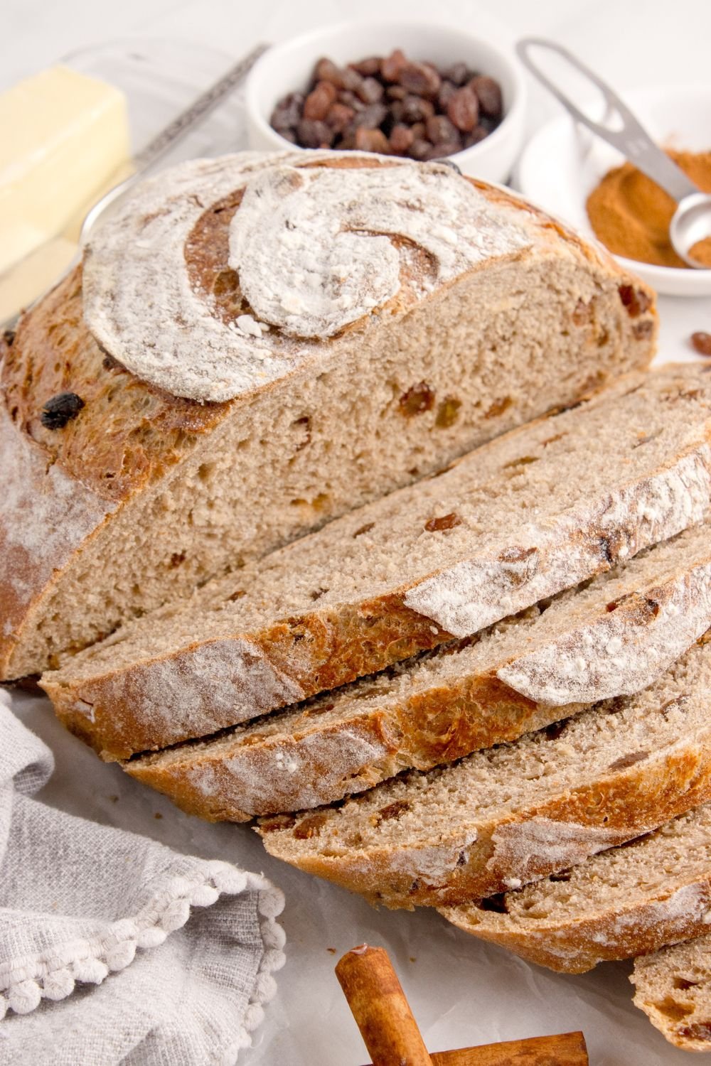 homemade cinnamon raisin bread partly sliced and sitting on table with some raisins in a bowl behind it