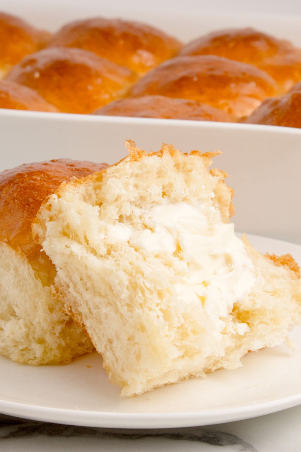pull apart dinner rolls in a pan with one on a plate slathered with butter 