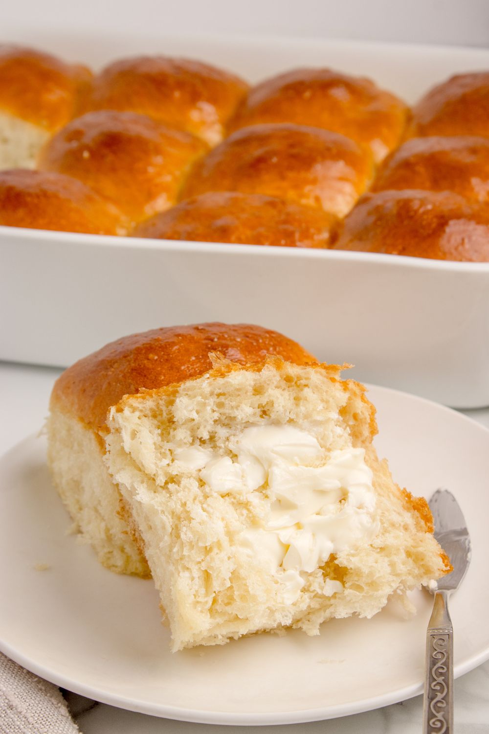 Pull Apart Rolls in a baking pan on counter with one cut in half spread with butter 