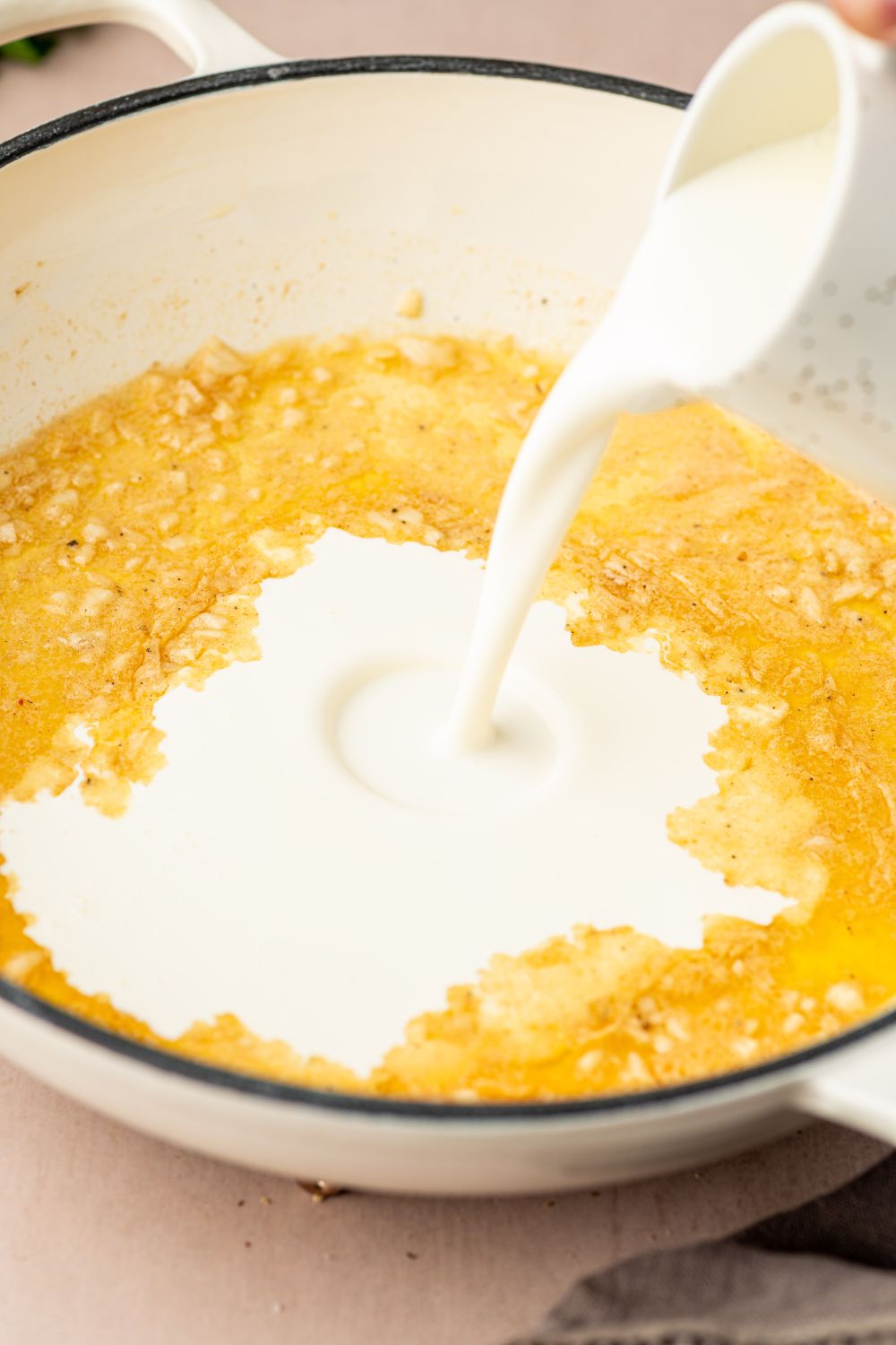 heavy cream being poured into skillet to make alfredo sauce 