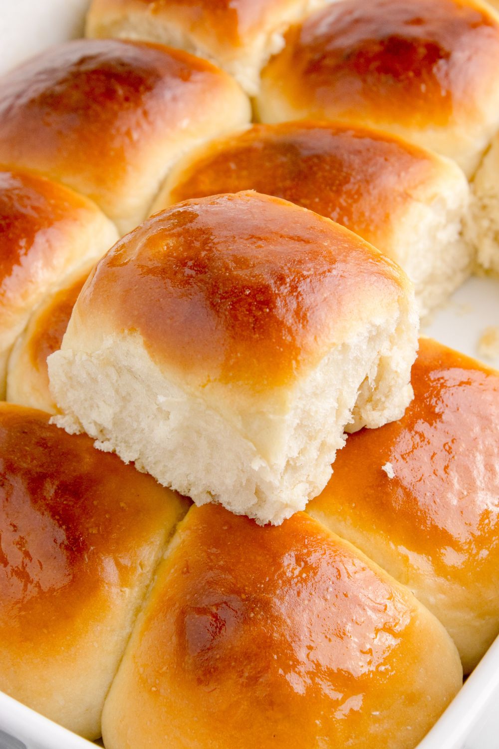 Hawaiian Dinner Rolls in a pan with one sitting on top of the pan to show the fluffy texture