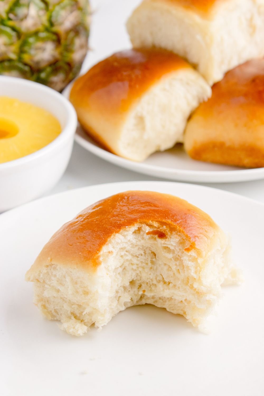 bite taken out of Hawaiian roll on plate with a pan of rolls behind it on table
