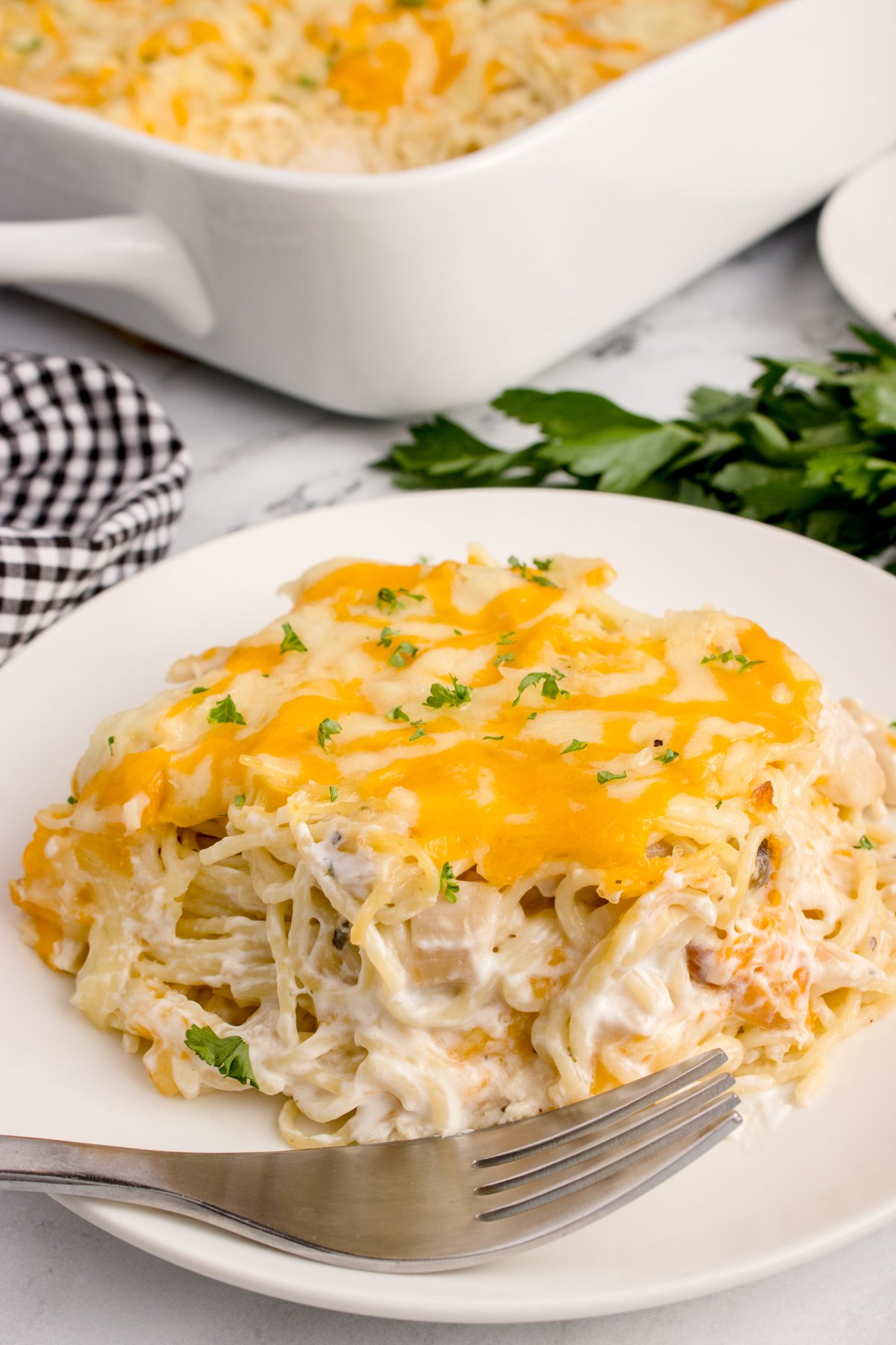 Chicken Tetrazzini on a plate with more in a casserole dish behind it on table 
