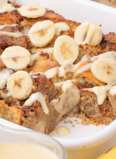 Banana Bread Pudding in a casserole dish with a glass of milk and bananas in front of the pan
