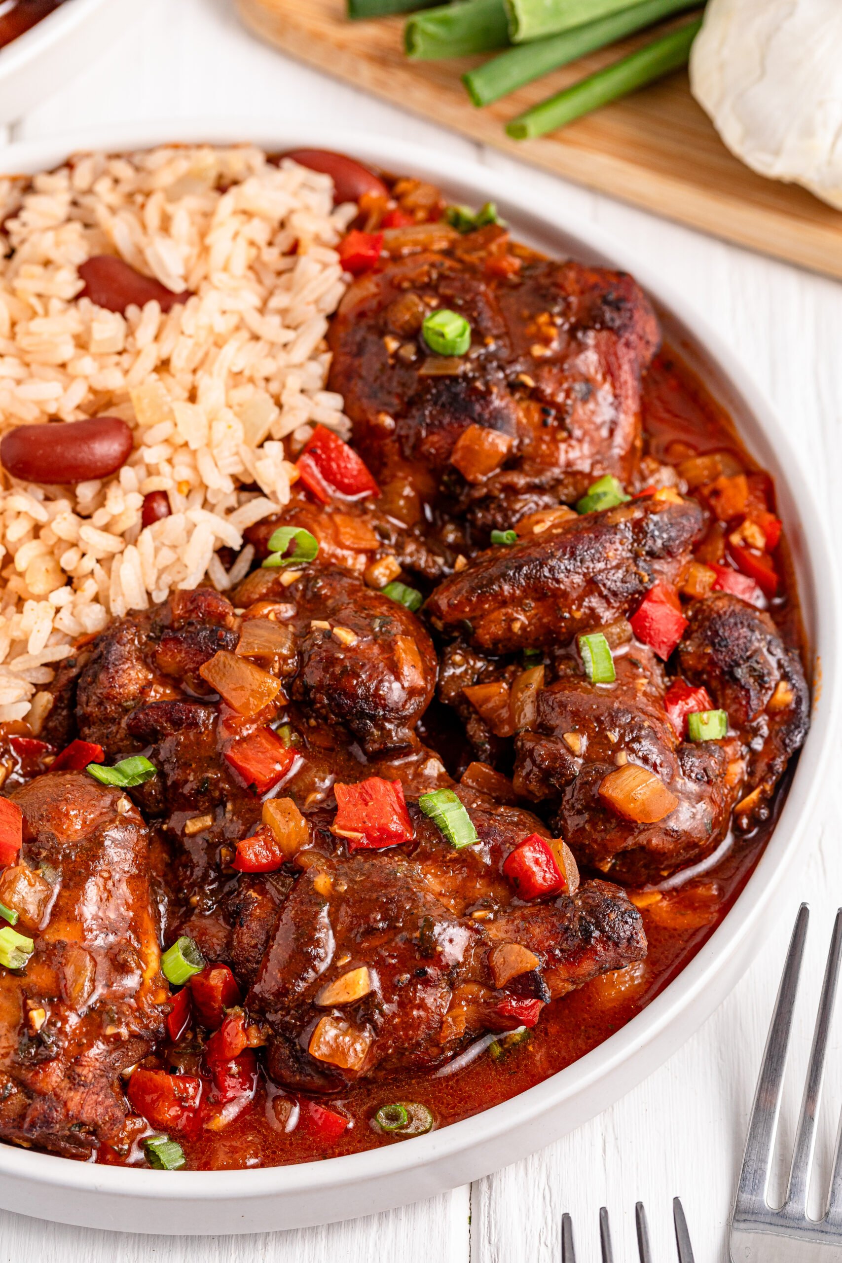 up close view of Jamaican Brown Stew Chicken in a white bowl with a side of rice and beans