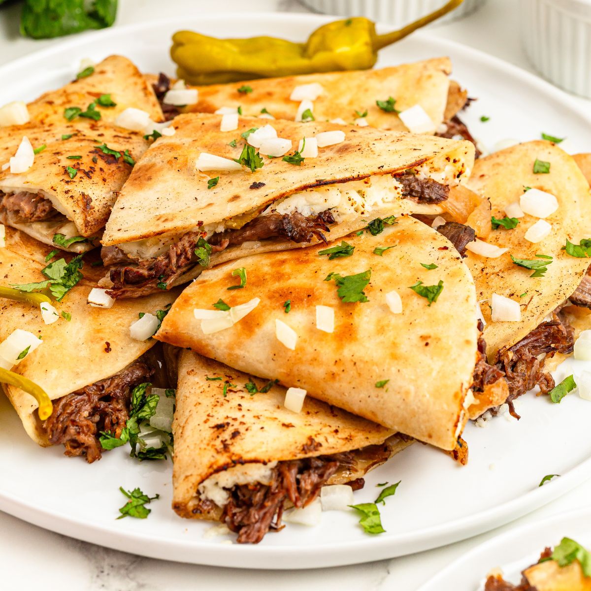Mississippi Pot Roast Quesadillas stacked on a plate with cilantro and onions on top