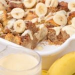 Banana Bread Pudding in a casserole dish with a glass of milk and bananas in front of the pan