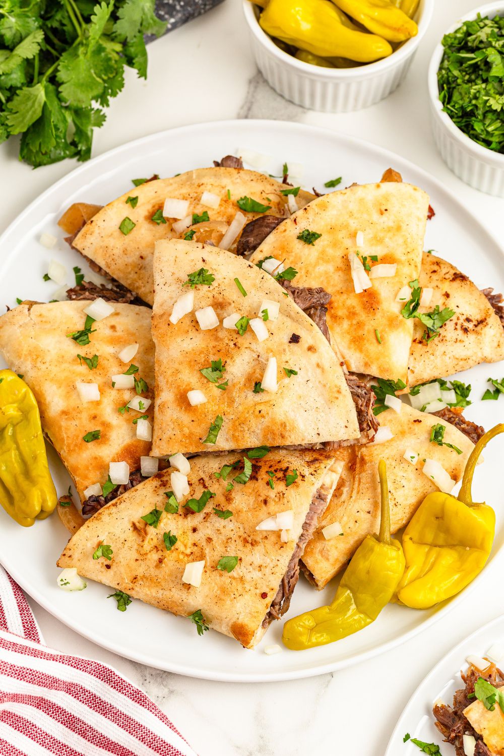 Mississippi Pot Roast Quesadillas piled on a plate with pepperocinni peppers around it 