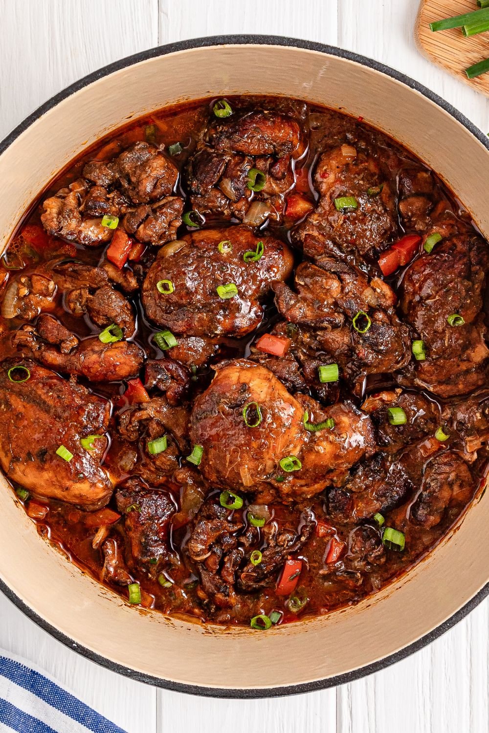 Jamaican Brown Stew Chicken in pot sitting on table with a towel to side 