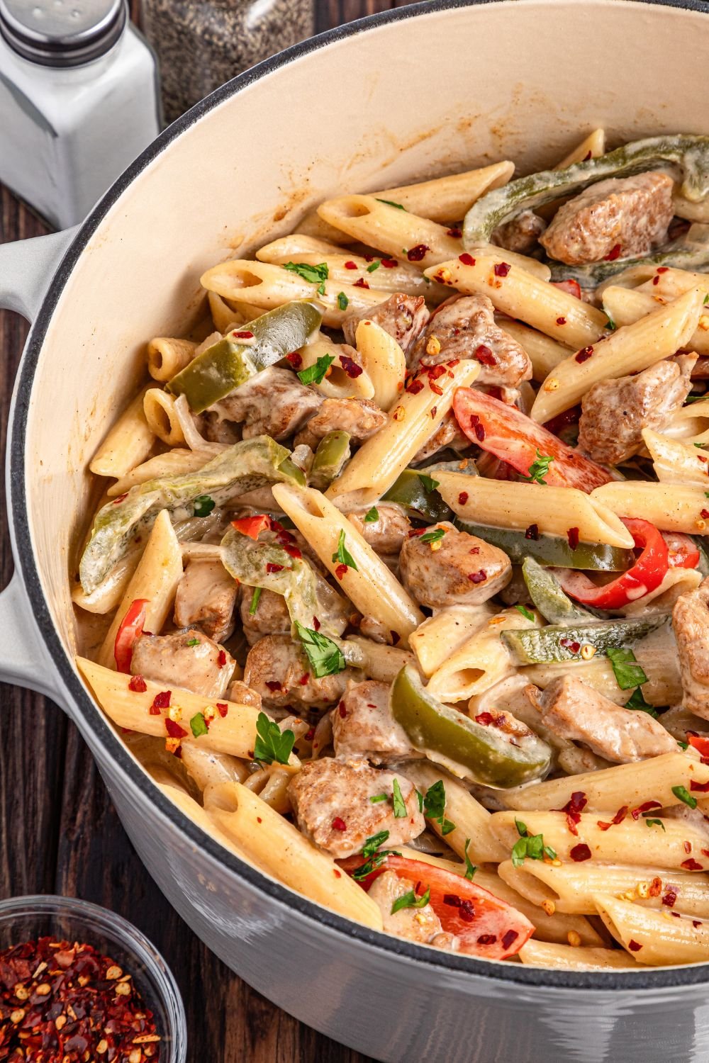 Rasta Pasta in a pot on table with a small bowl of red pepper flakes to the side of pot