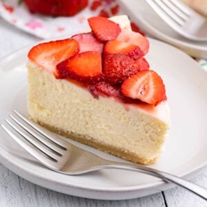 slice of keto cheesecake on a plate topped with strawberries and fork on the side of plate