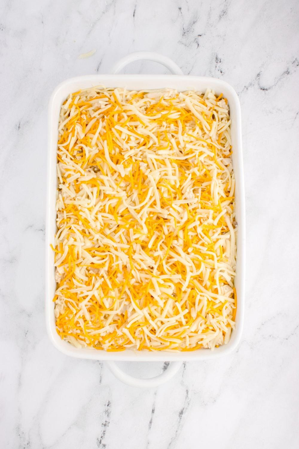 shredded cheese spread out over pan with chicken tetrazzini in pan