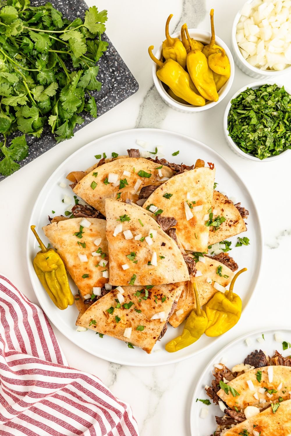 plate with beef quesadillas on them with peppers, onions, and more around the table