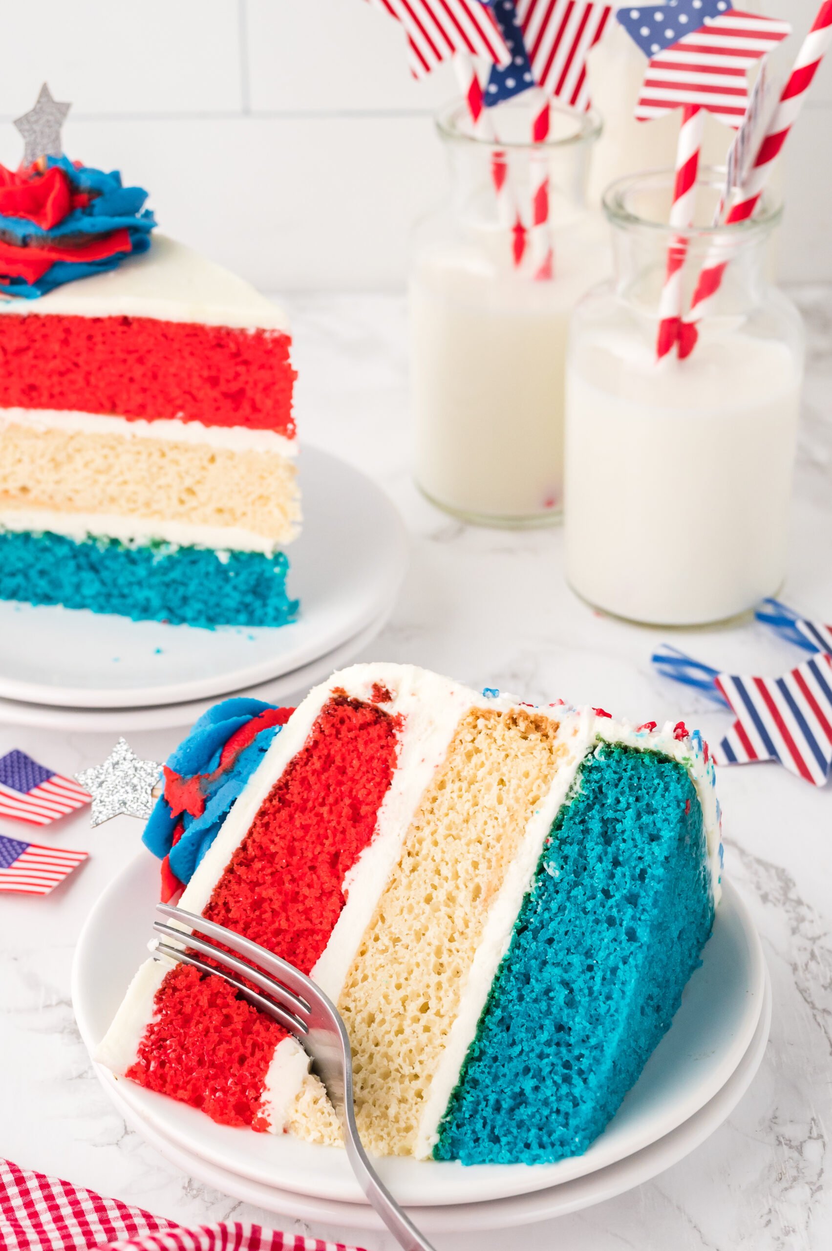 Slice of American Flag Layered Cake on a white plate with cups of milk behind the cake