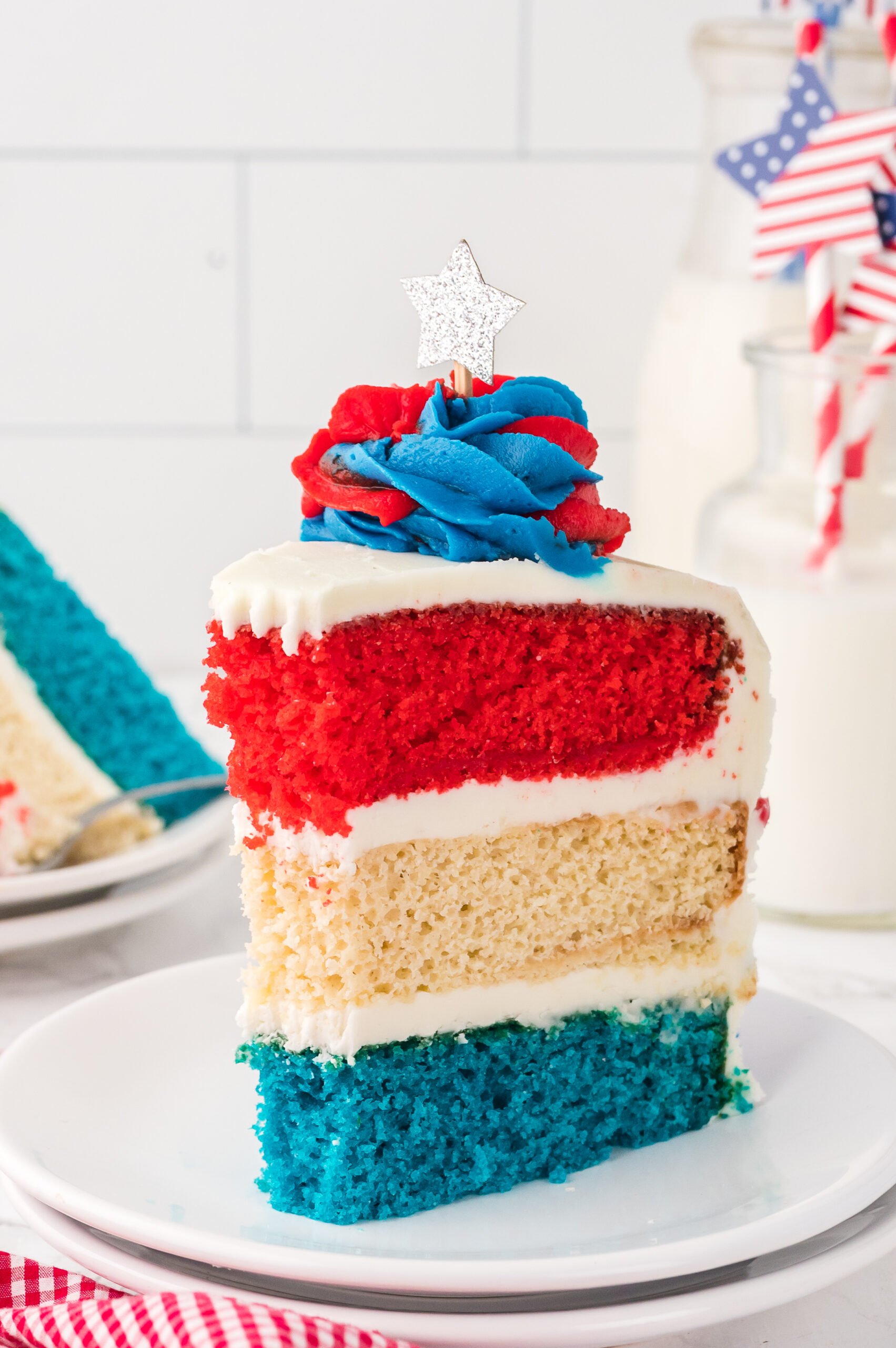 Slice of American Flag Layered Cake on a white plate with cups of milk behind the cake
