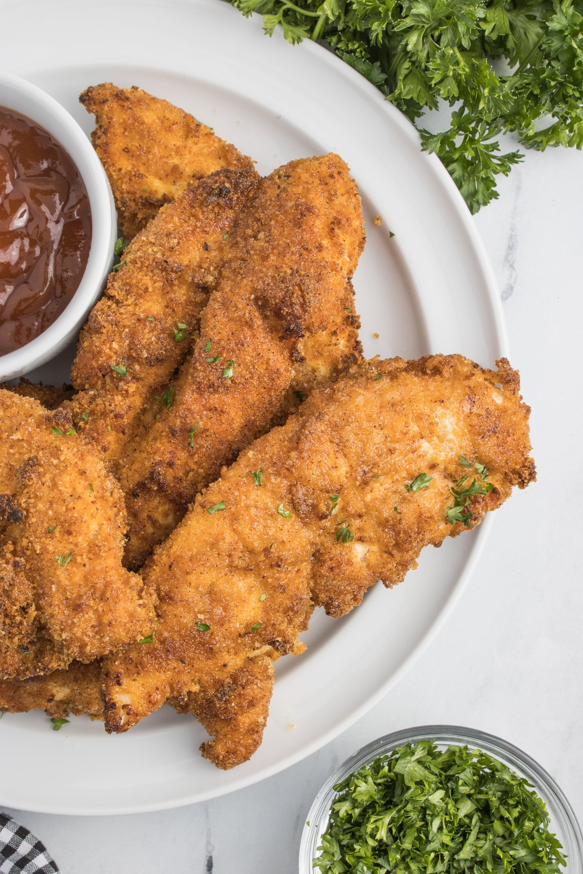 Air Fryer Chicken Tenders on a white plate with a small cup of BBQ sauce on the side 
