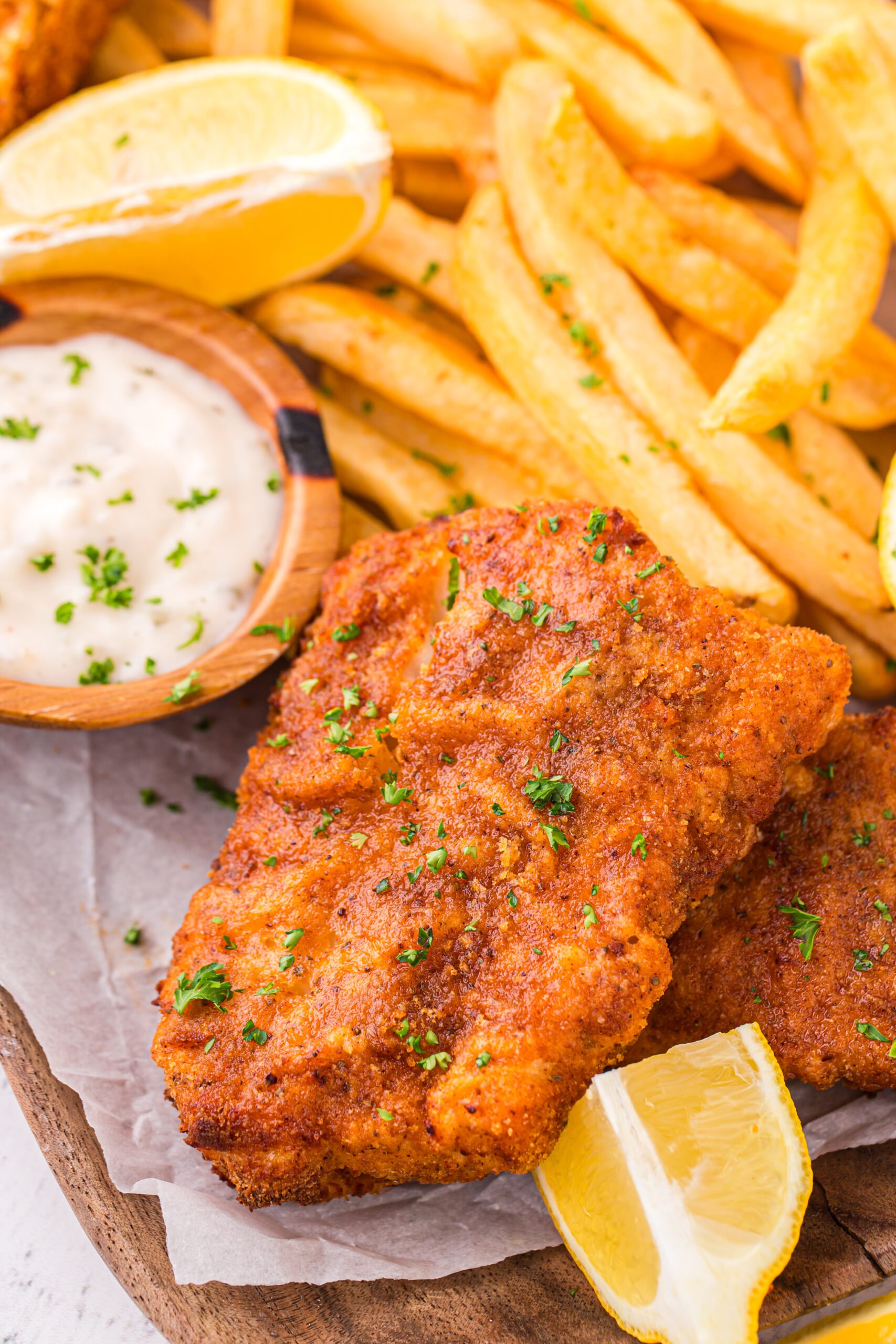 Up close shot of the Air Fryer Fish And Chips on a platter with fries and lemon wedges and tartar sauce on side