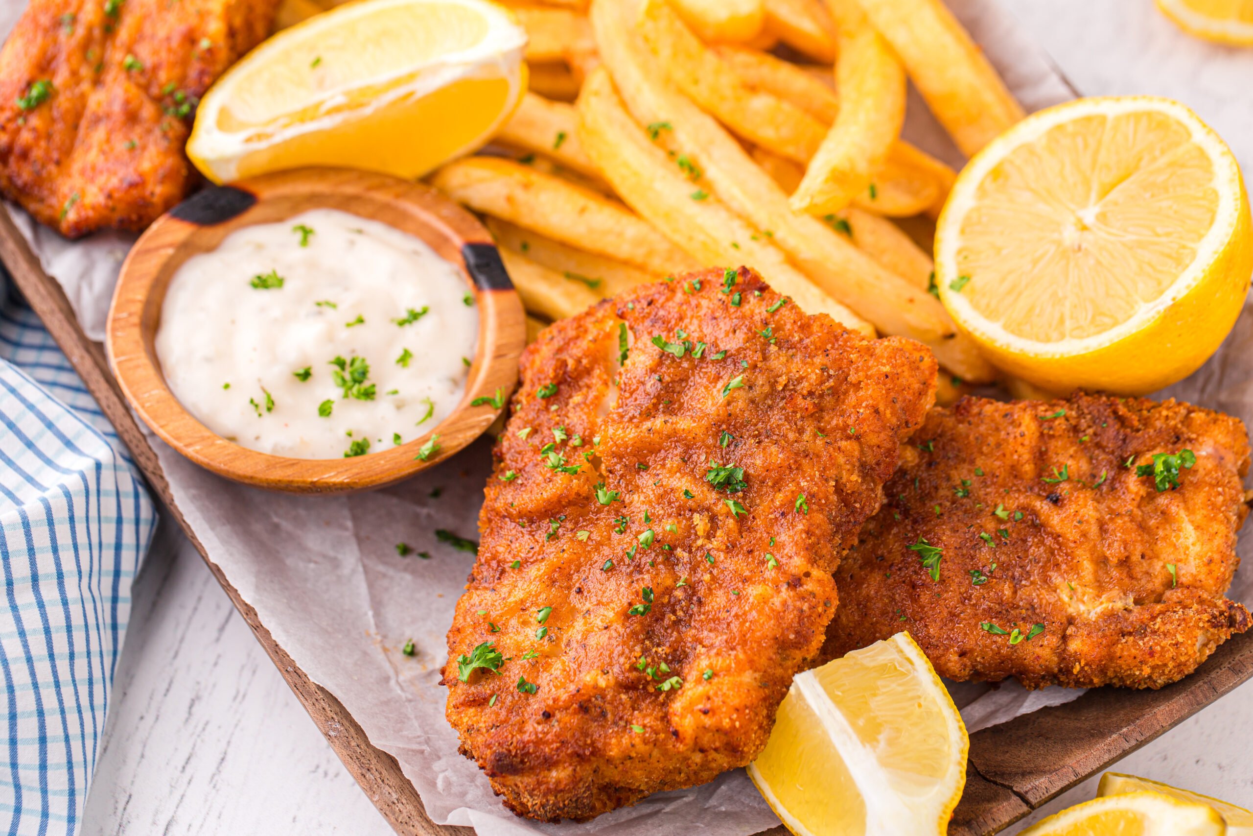 Up close shot of the Air Fryer Fish And Chips on a platter with fries and lemon wedges and tartar sauce on side