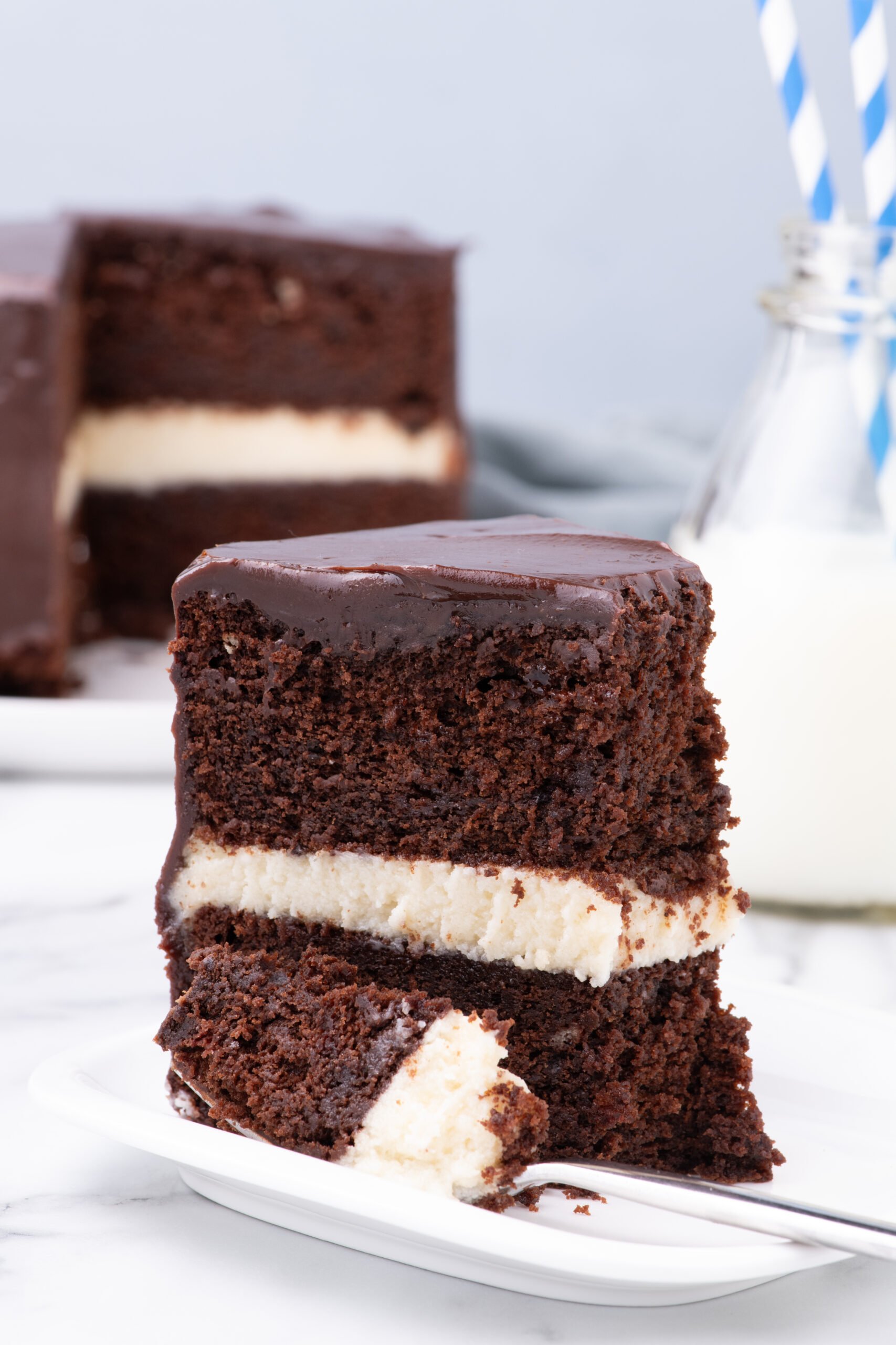 Slice of Ding Dong Cake on a white plate with the whole cake in the background 