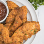 Air Fryer Chicken Tenders on a white plate with a small cup of BBQ sauce on the side
