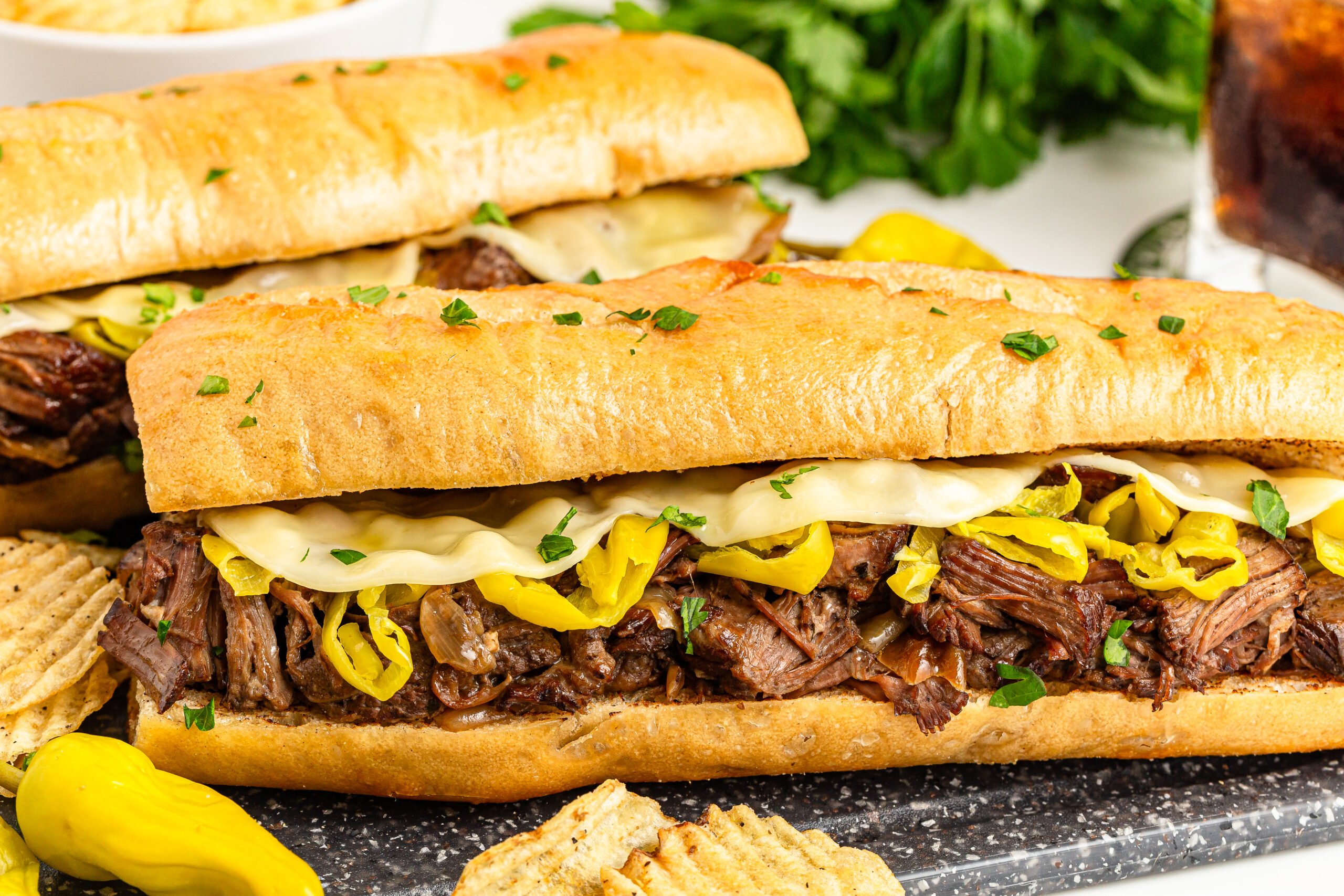 side view of Two Mississippi Pot Roast Sandwiches on a cutting board with chips on the side 