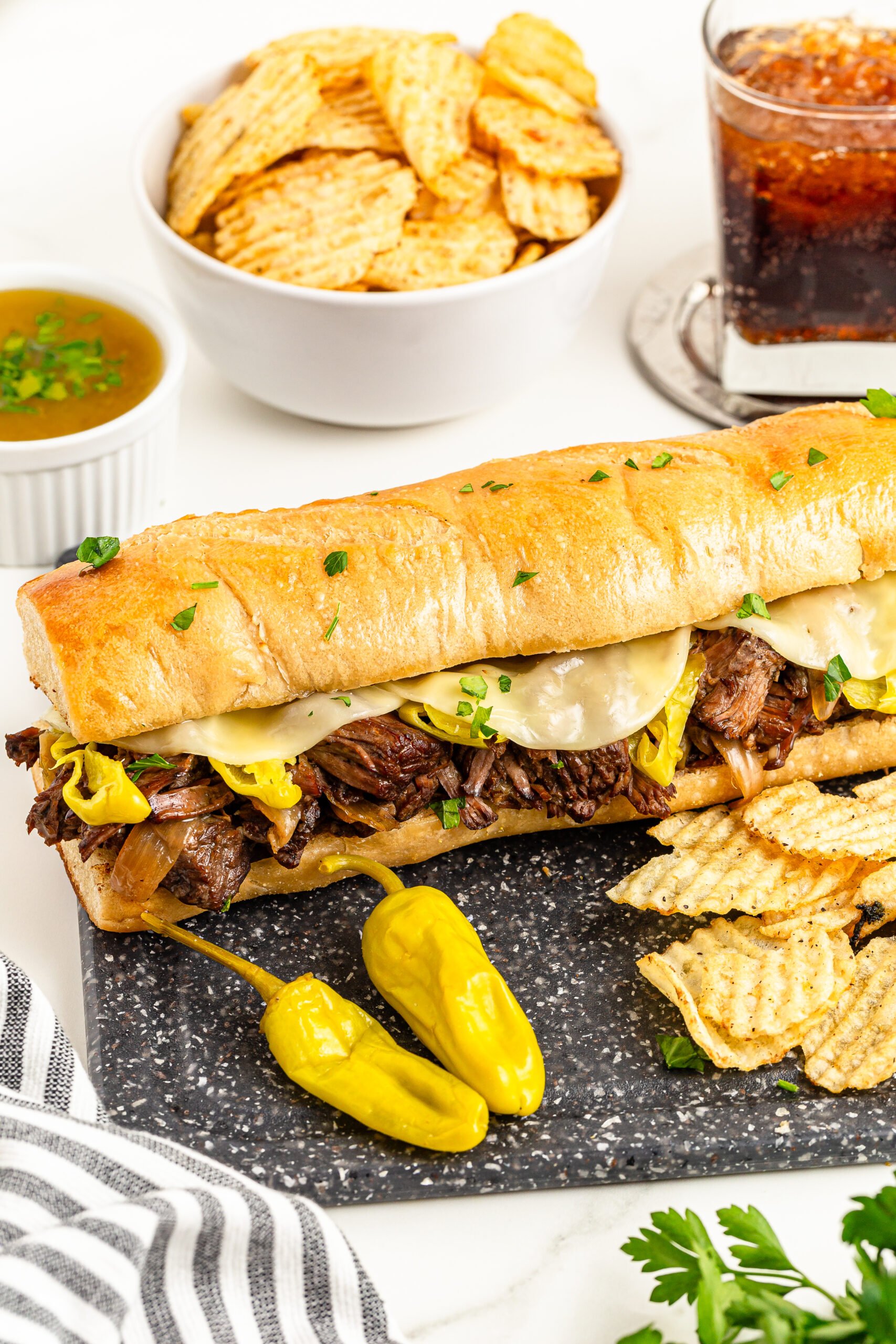 One Mississippi Pot Roast Sandwich on a cutting board with chips on the side and a soda