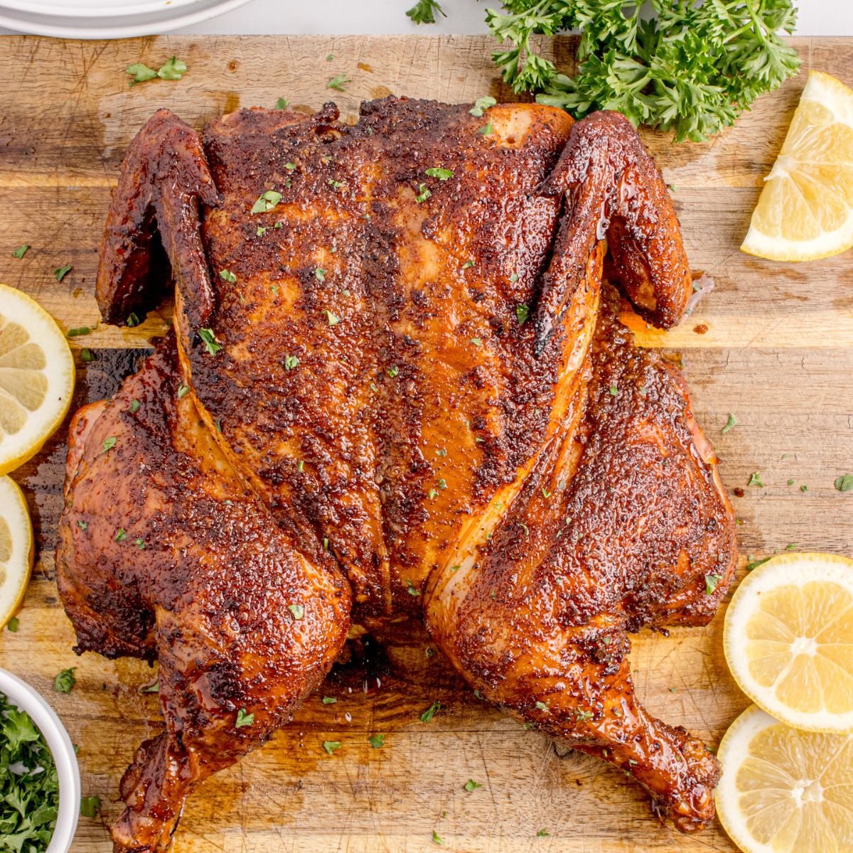 Smoked Whole Chicken  on a cutting board with lemon wedges to side 