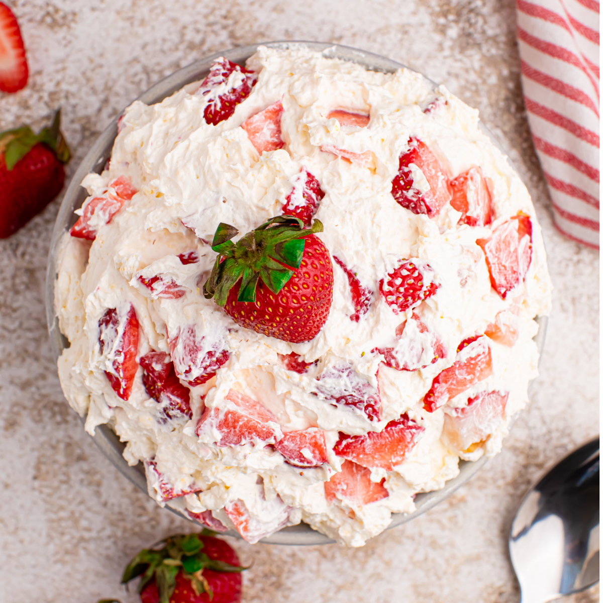 Overhead view of the strawberry cheesecake salad in a white bowl with a fresh strawberry on top. 